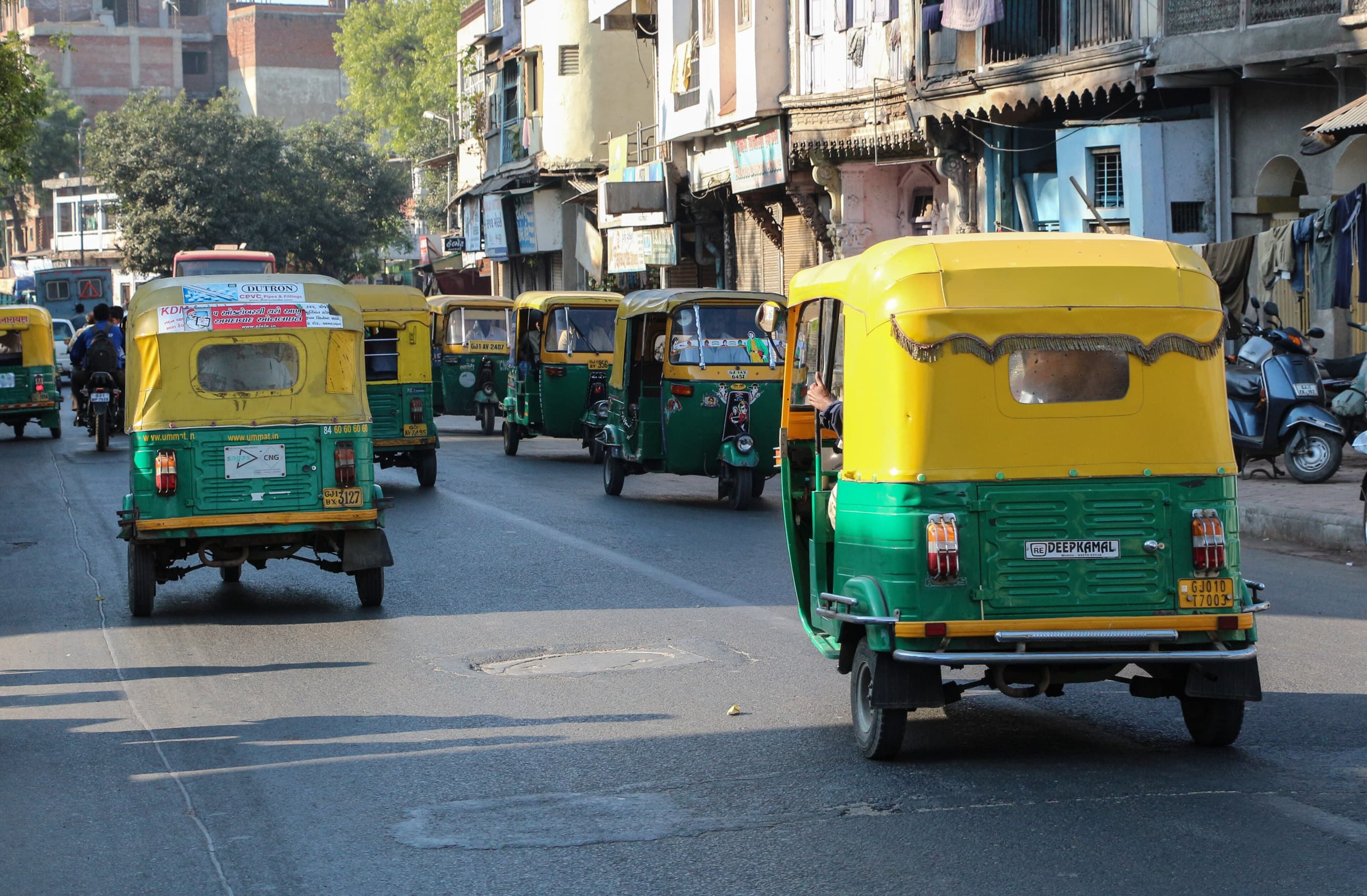 Green and yellow auto-rickshaws in city traffic.
